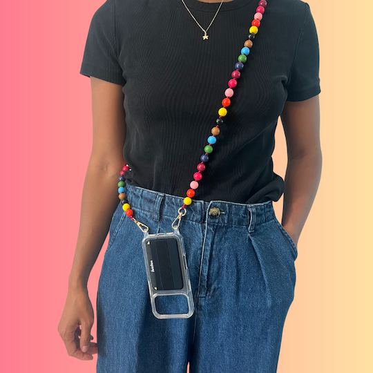 Person wearing a colorful beaded phone lanyard with a clear case on a pink and orange gradient background