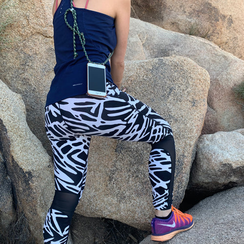 Woman hiking in leggings and a top on a rocky hillside, wearing a Keebos crossbody phone case